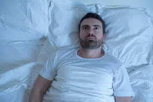 man laying awake unable to sleep due to sleep apnea